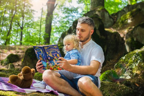 A parent reading a picture book with their child while sitting outdoor